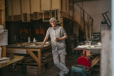 Smiling senior craftsman leaning on workbench at carpentry workshop