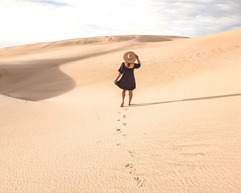 Rear view of man walking on sand at desert
