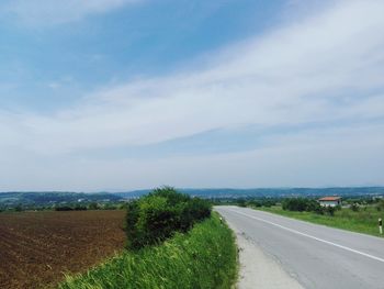 Empty road amidst field against sky