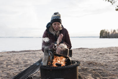 Woman warming up by a campfire on the beach in sweden