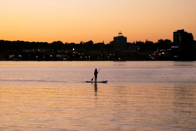 Scenic view of paddle boarder on the water against sky during sunset