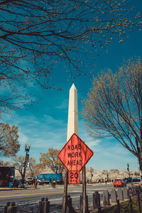 Road sign by street against washington monument in city