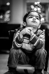 Cute boy looking up while sitting on small chair at home