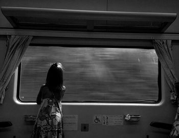 Rear view of girl looking through window while traveling in train