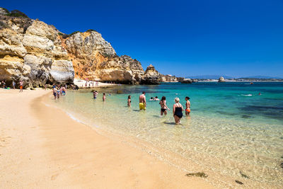 People on shore at beach against clear blue sky