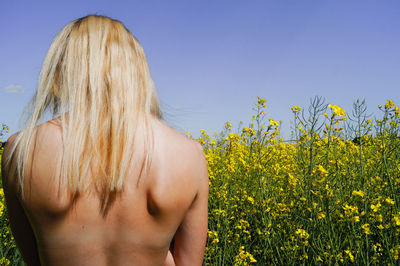 Rear view of shirtless man standing on field against clear sky