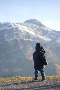 Rear view of man standing on snowcapped mountain against sky