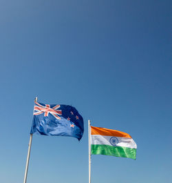 The new zealand and indian flags flutter in the wind under a clear blue sky