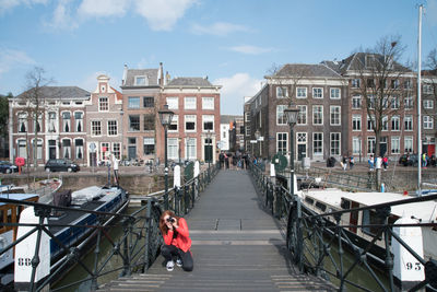 People walking on canal amidst buildings in city against sky