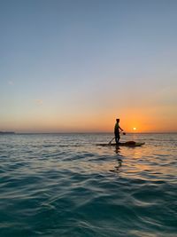 Silhouette person in sea against sky during sunset