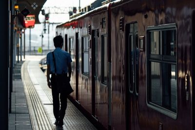 Rear view of man walking by train at railroad station