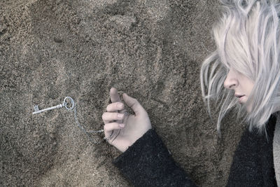 Directly above shot of young woman holding key pendant while lying on sand