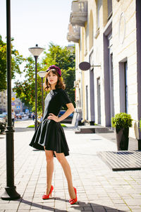 Beautiful young woman in black dress standing on sidewalk in city