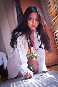 Portrait of young woman with red rose kneeling on floor