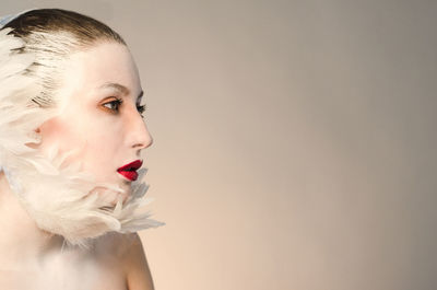 Close-up of young woman with make-up and feathers against gray background