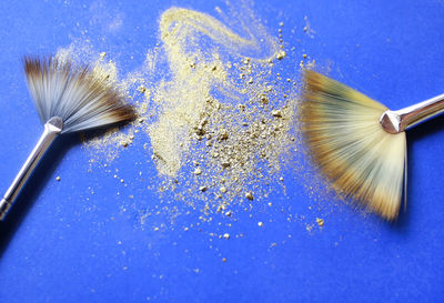 Directly above shot of make-up brushes with glitter on blue table