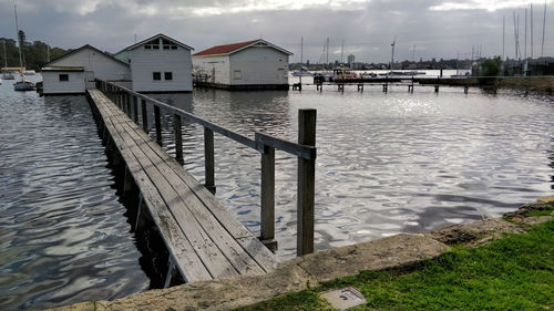 Pier on lake by houses against sky