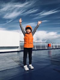 Full length of cute boy standing with arms raised on pier