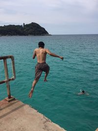 Rear view of shirtless man jumping in sea