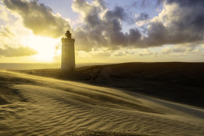 Lighthouse by sea against sky during sunset