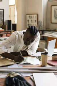 Male designer writing on paper at desk in workplace