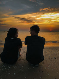 Rear view of couple sitting on beach during sunset