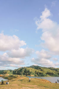 People relaxing on land amidst lake against sky