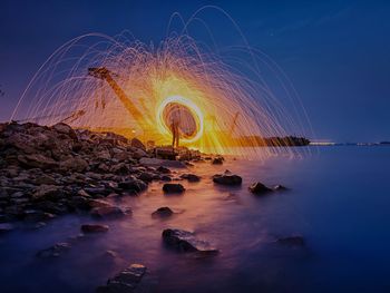 Person spinning wire wool by sea at night