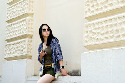 Portrait of young woman standing against wall