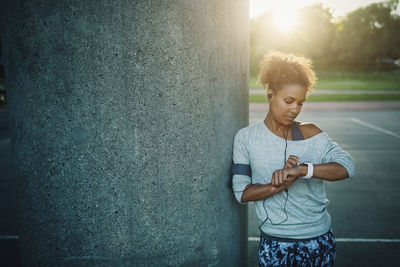 Woman using smart watch while standing by column