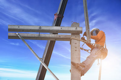 Low angle view of man working against blue sky