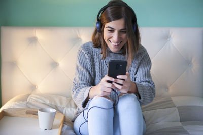 Smiling woman using smart phone while sitting on sofa