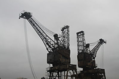 Low angle view of cranes at construction site against sky