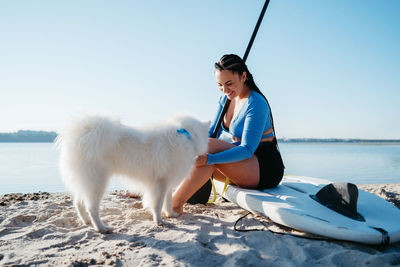 Cheerful woman with dreads preparing to paddleboarding with her snow-white dog breed japanese spitz