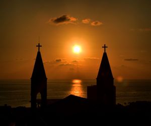 Silhouette church by sea against sky during sunset