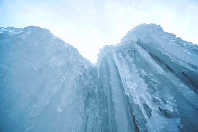 Low angle view of icicles on snow covered landscape against sky