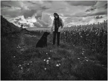 Woman standing on field against sky with black labrador