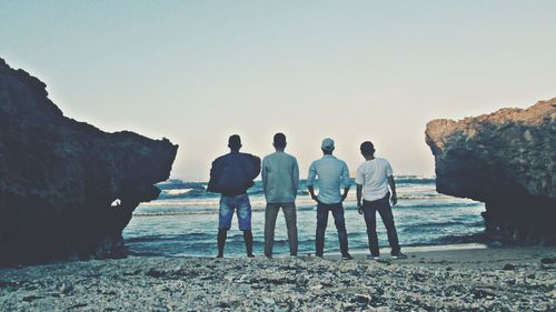 Rear view of people standing on beach against clear sky