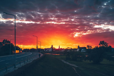 Cars on road against dramatic sky during sunset