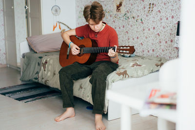 A teenage girl plays the acoustic guitar while sitting in her room.