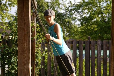 Portrait of teenage boy swinging against trees in park