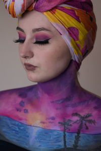 Close-up of beautiful young woman with make-up and body paint against wall