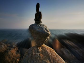 Stack of stones on rock by sea against sky