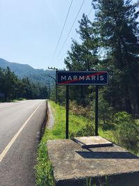 Road sign by trees against sky