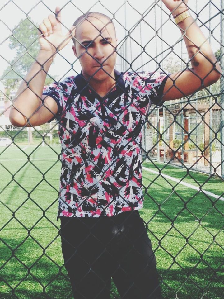 lifestyles, leisure activity, person, standing, casual clothing, front view, fence, chainlink fence, childhood, grass, protection, focus on foreground, portrait, looking at camera, three quarter length, day, safety, young adult