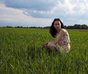 Thoughtful young woman crouching on grassy field