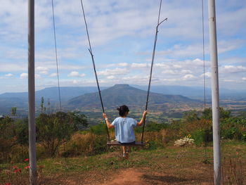 Rear view of woman sitting on rope swing against sky