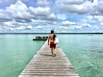 Rear view of woman standing on pier over sea against sky