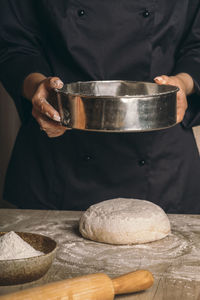 A woman sifts flour through a sieve over the dough close-up. the cook prepares bread dough