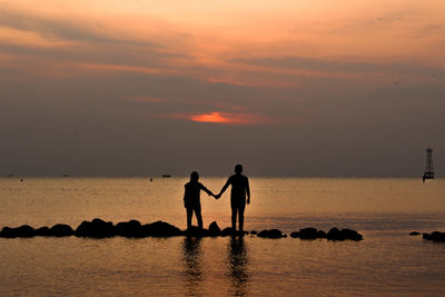 Silhouette couple standing at beach against sky during sunset